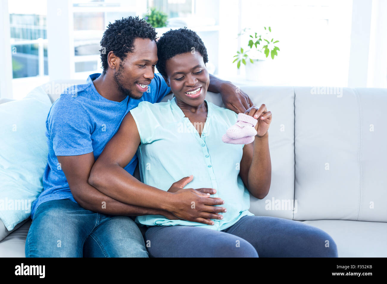Happy pregnant woman holding baby shoes while sitting on sofa Stock Photo