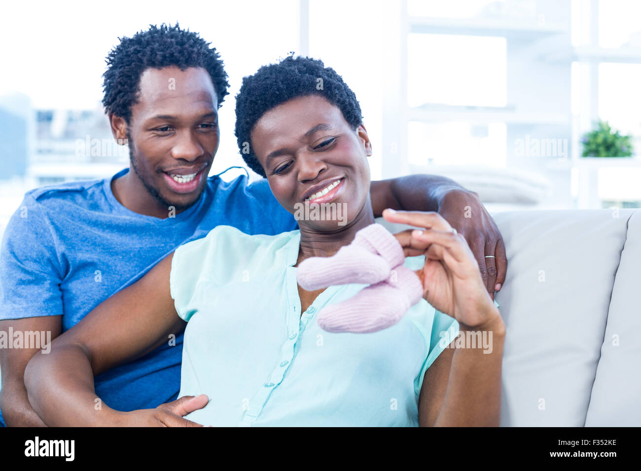 Happy couple looking at baby shoes while sitting on sofa Stock Photo