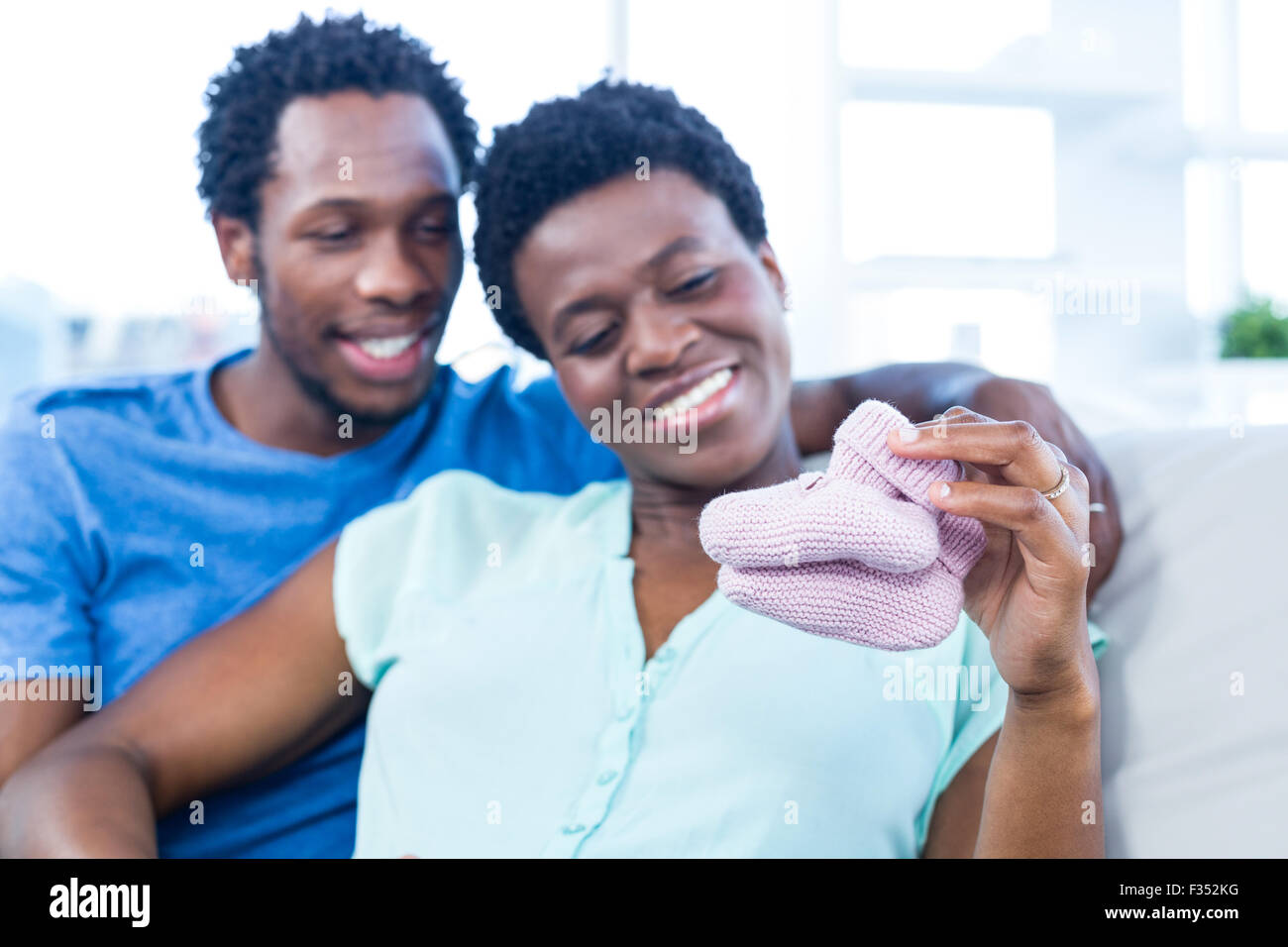 Couple looking at baby shoes while resting on sofa Stock Photo