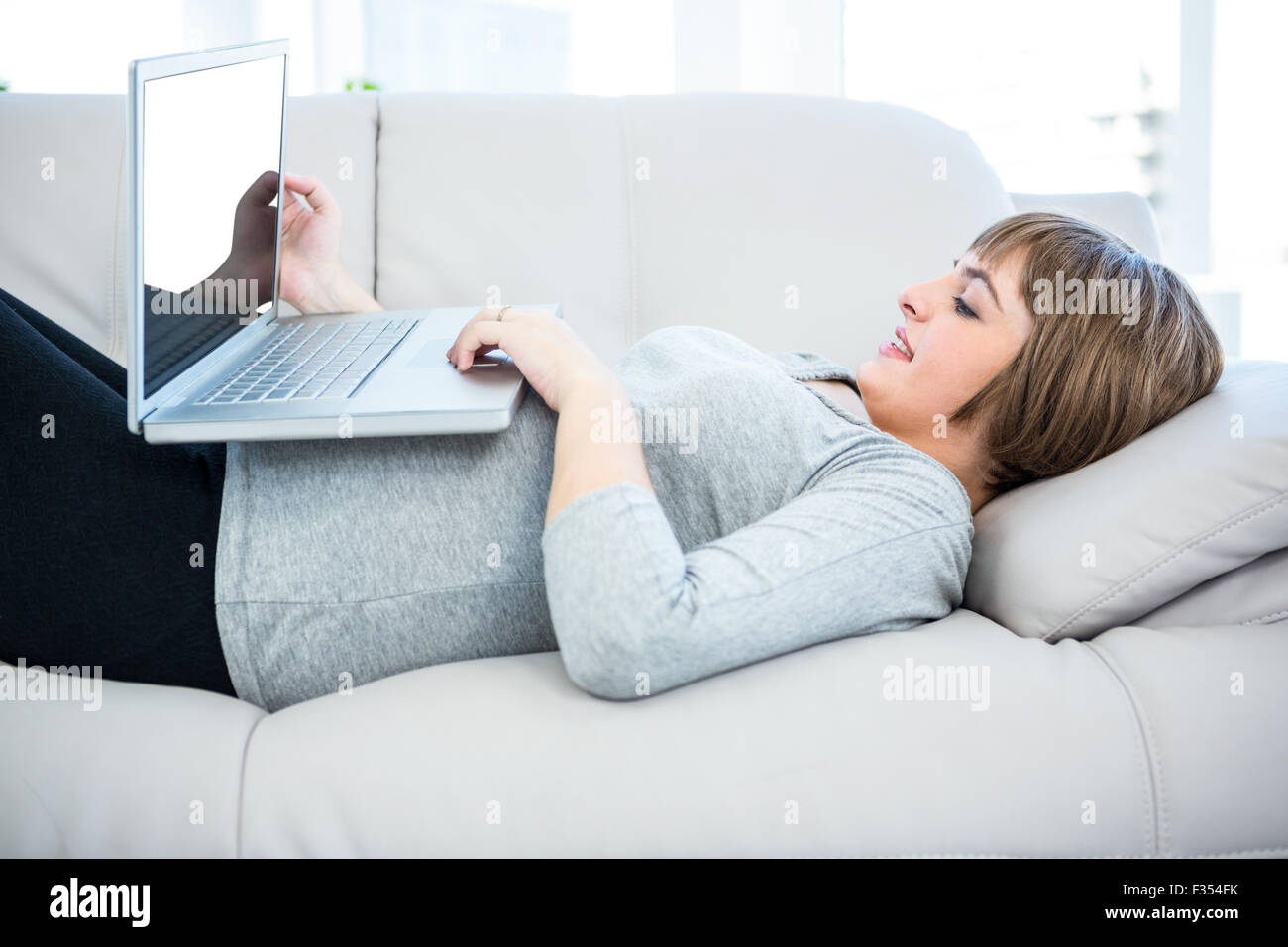 Smiling woman using laptop while lying on sofa Stock Photo - Alamy