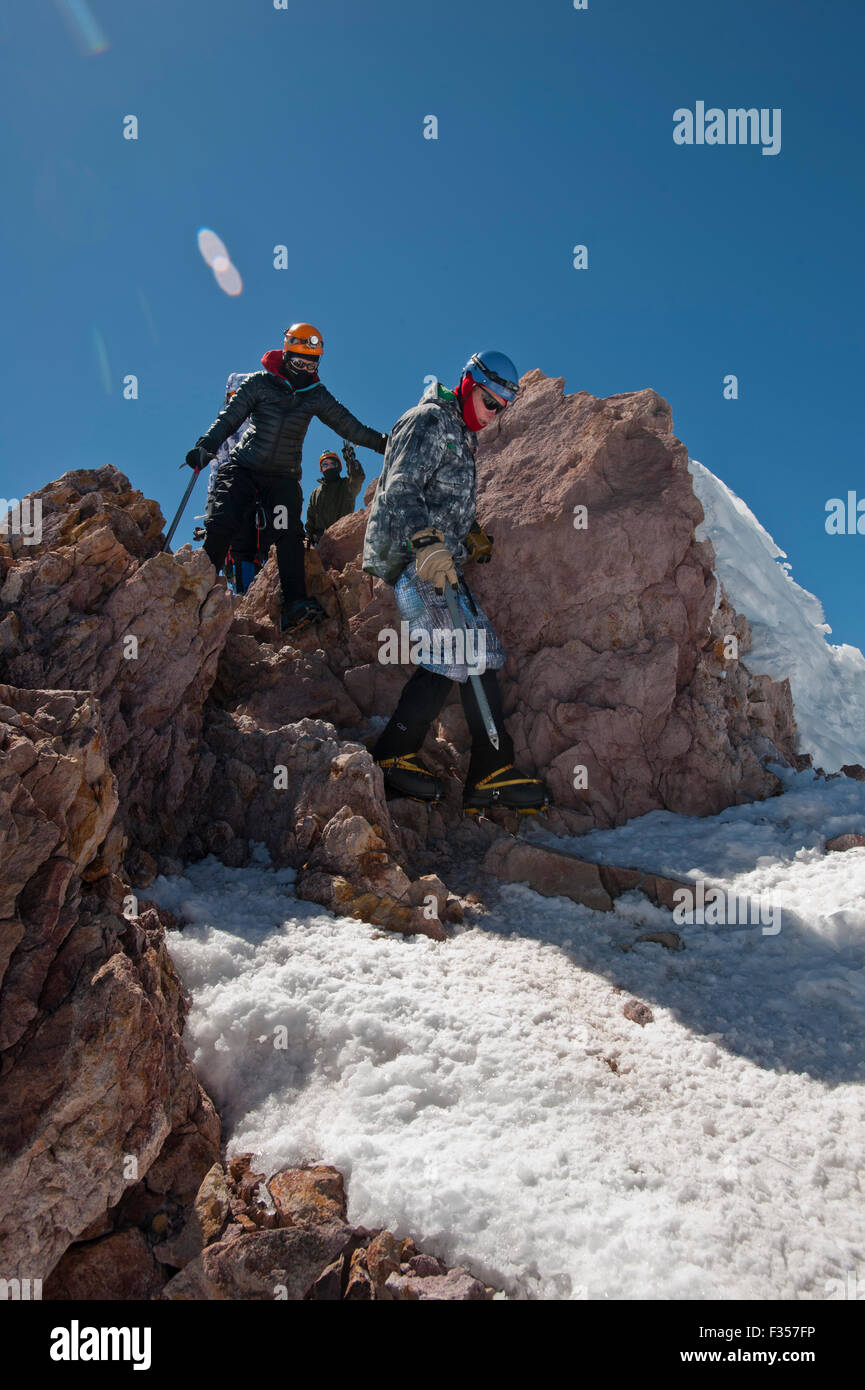 Three people climb down rocks on their descent from the summit of Mount
