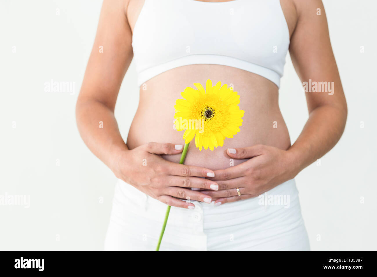 Pregnant woman touching her stomach while holding yellow flower Stock Photo
