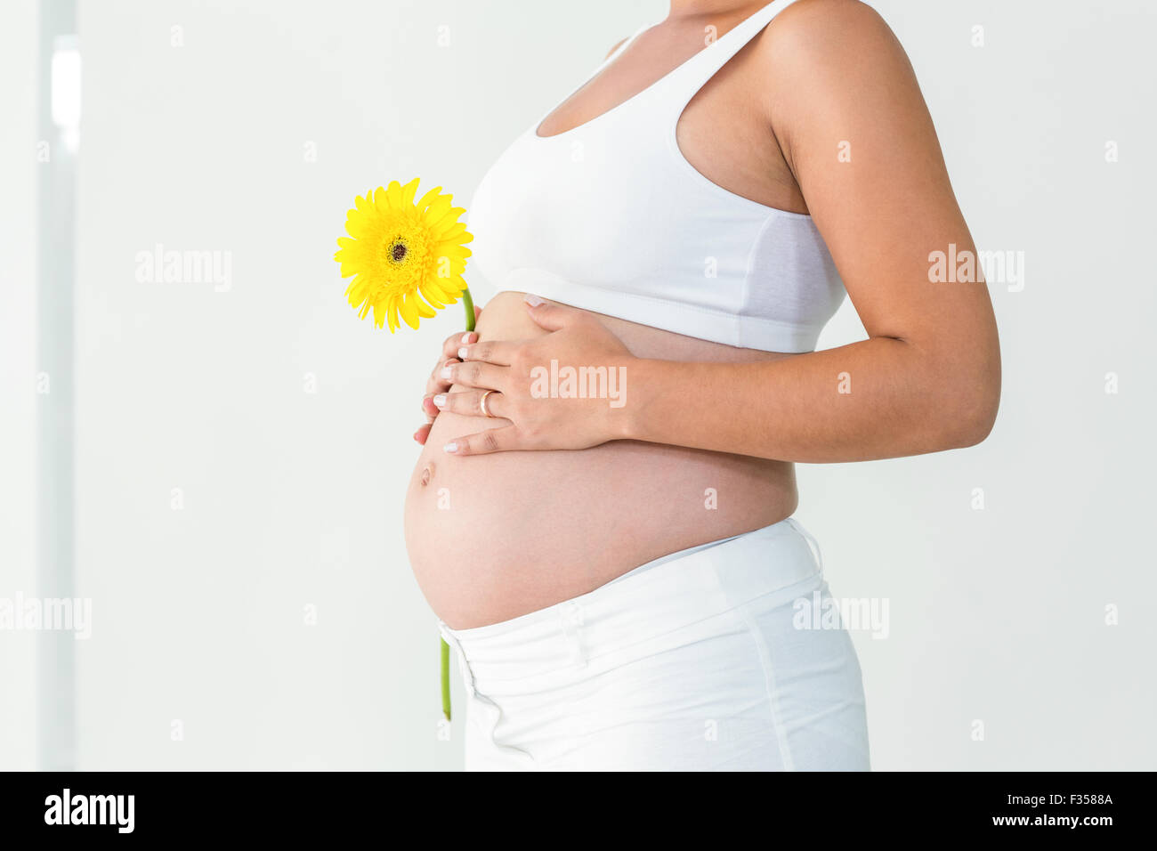 Pregnant woman touching her belly while holding yellow flower Stock Photo