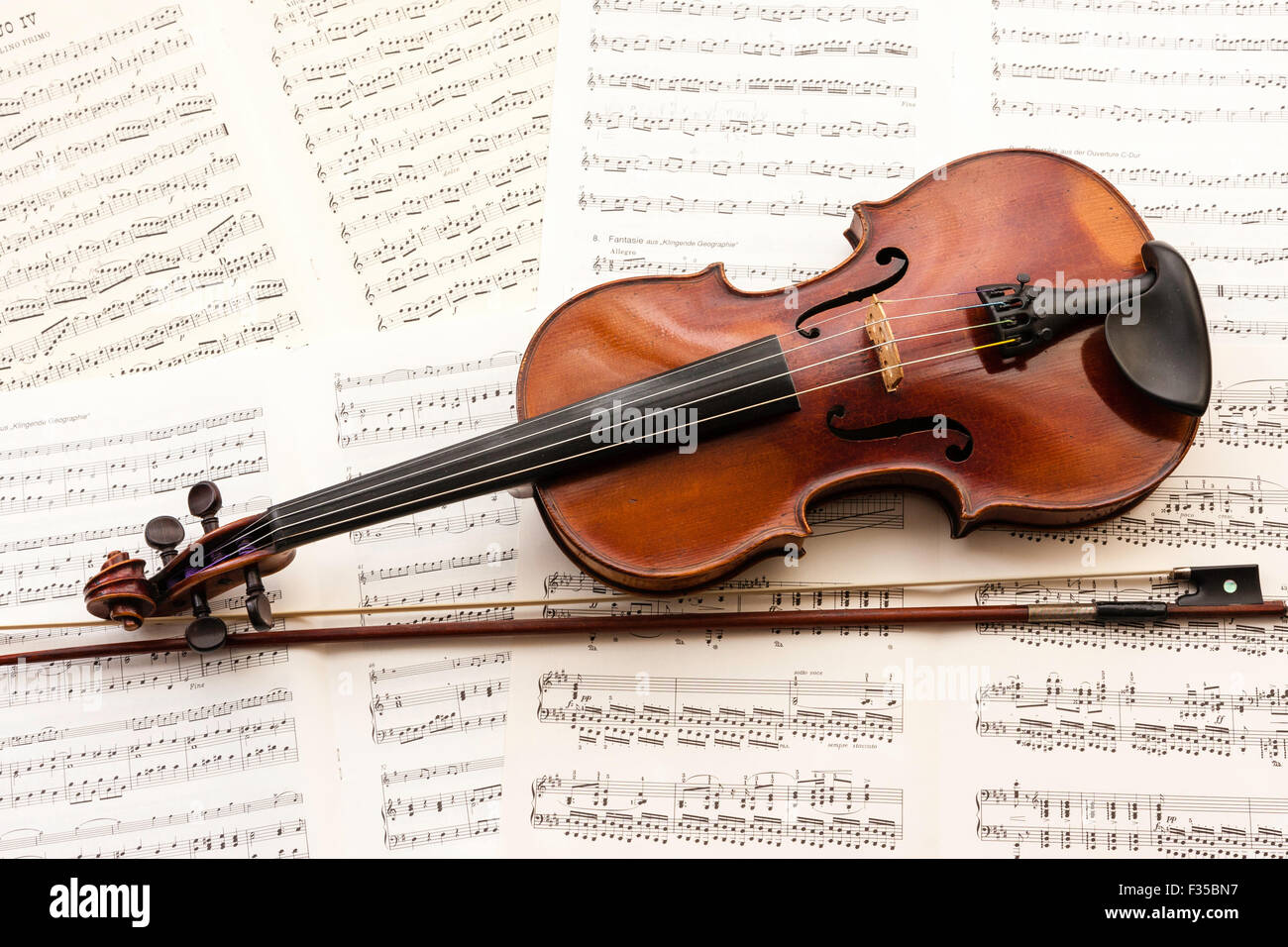 A restored violin marked Thouvenel, Paris, from circa 1800, with a vuillaume bow next to it, resting on a background of sheet music. Stock Photo