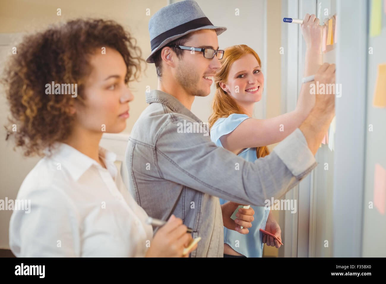 Businesswoman writing on adhesive notes on glass wall with colleagues Stock Photo
