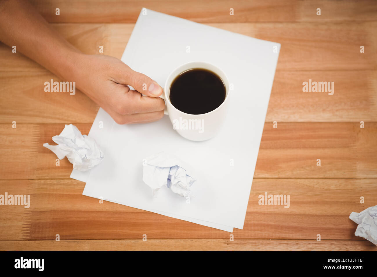 Man holding black coffee cup on paper at desk Stock Photo