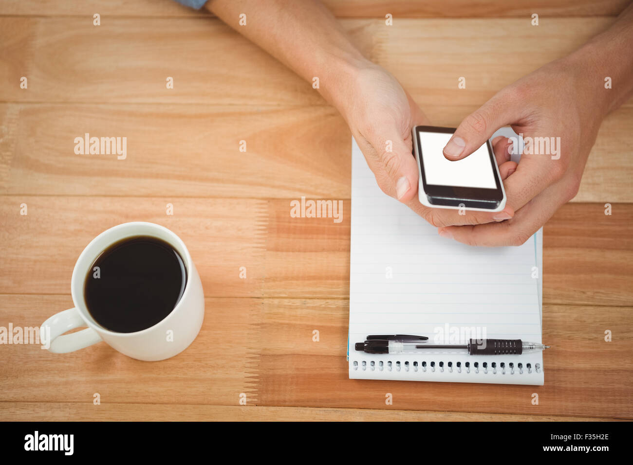 Hipster using smartphone with coffee and notepad on table in office Stock Photo