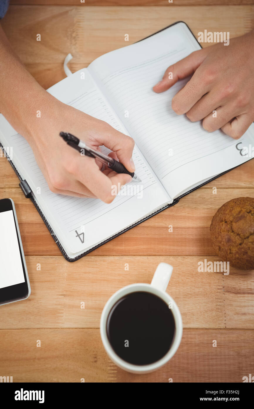 Man writing on diary with muffin and coffee at desk Stock Photo