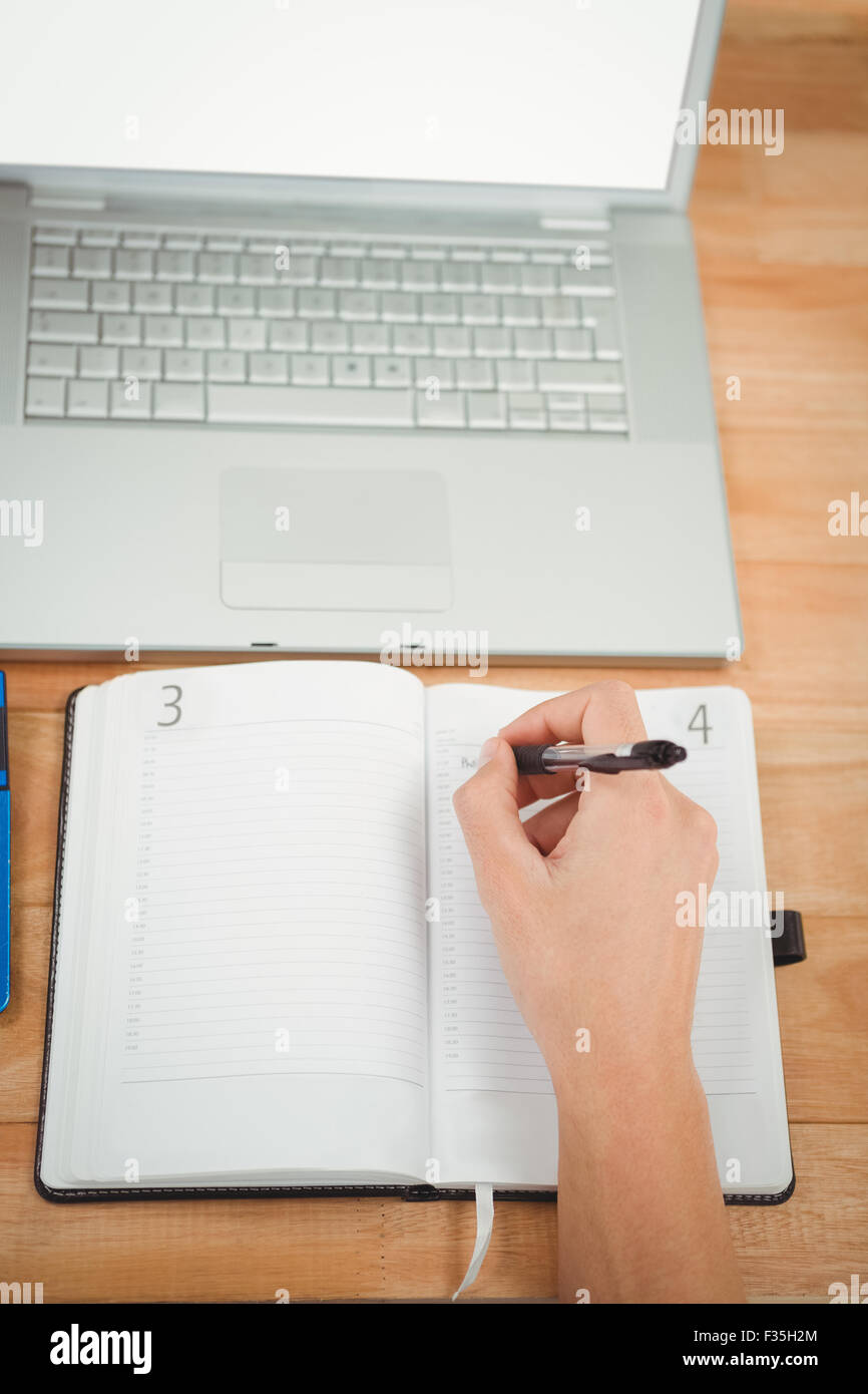 Man writing in diary while laptop at desk in office Stock Photo
