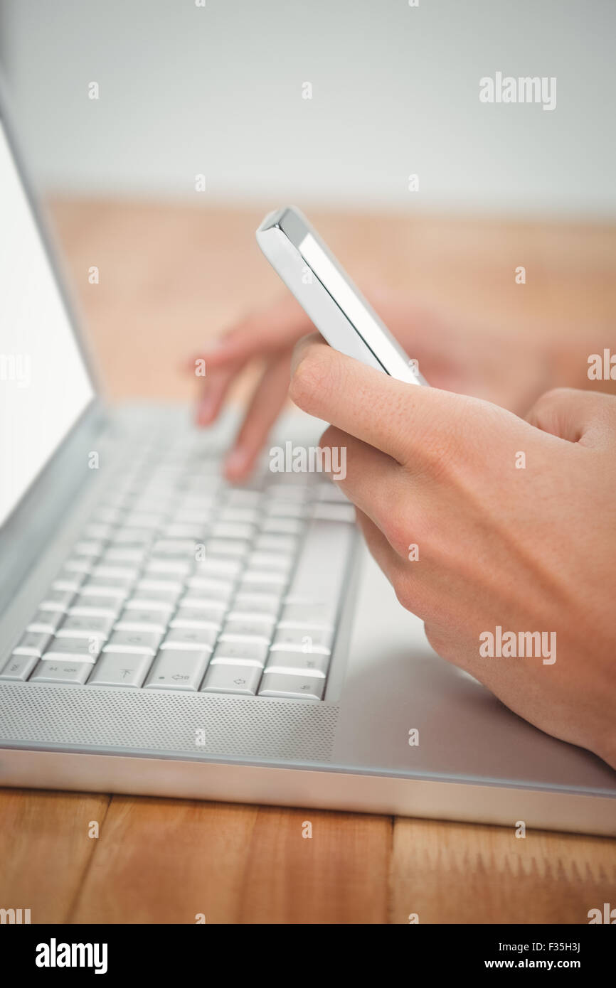 Man using mobile phone while typing on laptop Stock Photo
