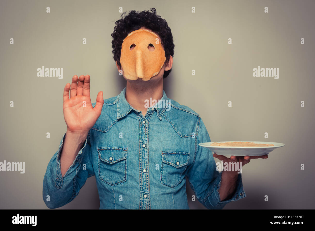 Young man has cut eyeholes in a pancake and is wearing it on his face