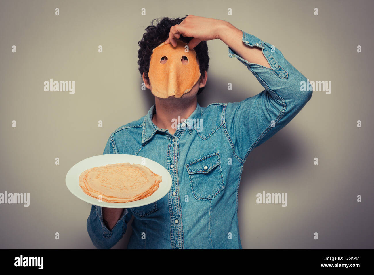 Young man has cut eyeholes in a pancake and is wearing it on his face