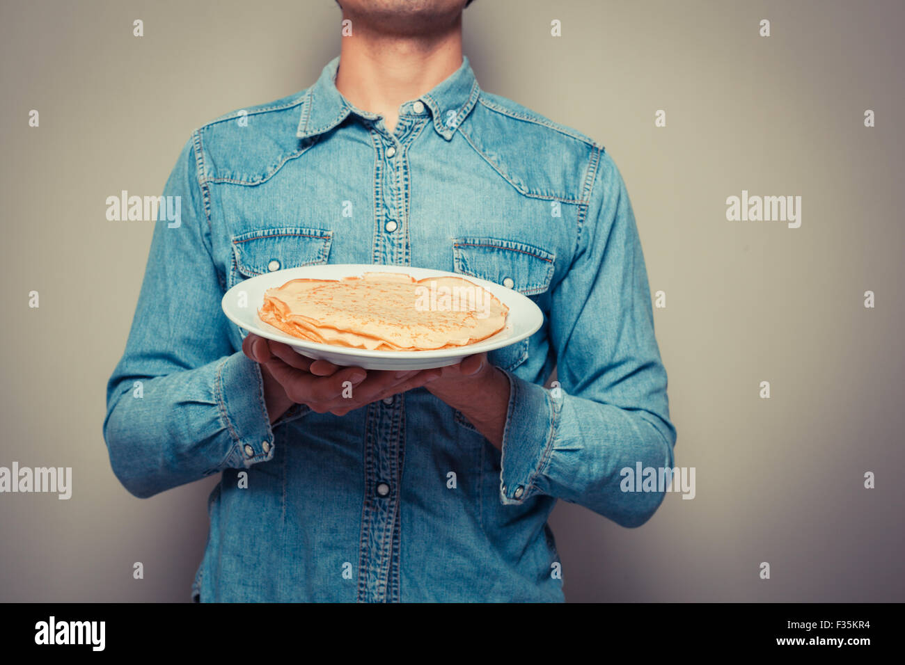 Young man is presenting a plate with a stack of pancakes Stock Photo