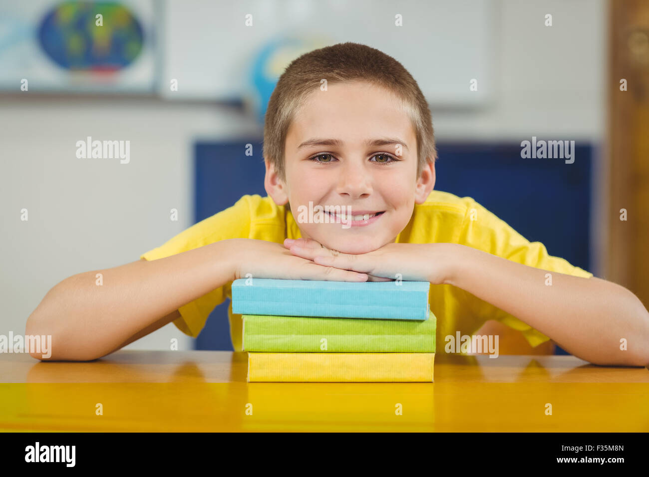 Smiling pupil leaning on pile of books in a classroom Stock Photo - Alamy