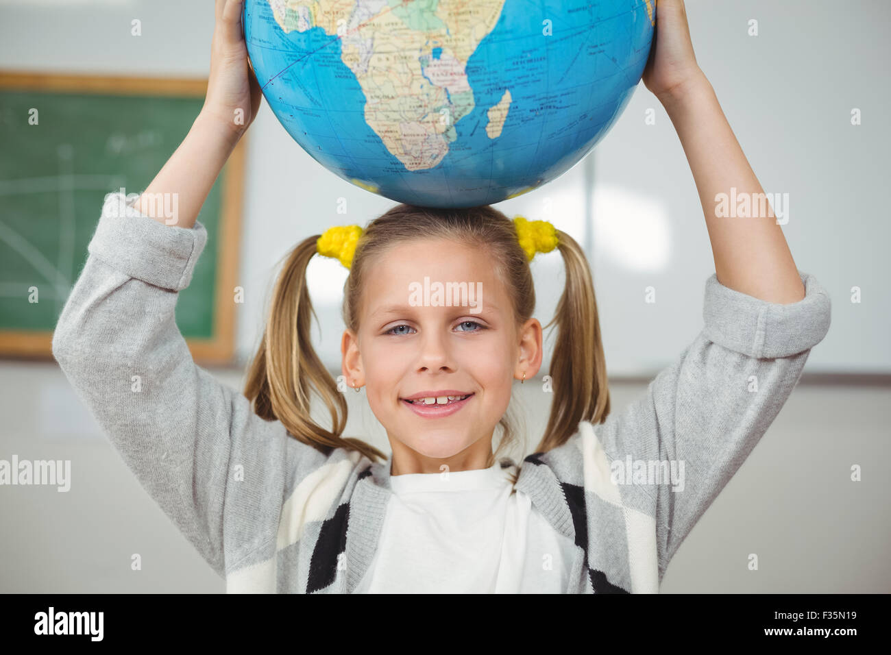 Cute pupil balancing globe on head in a classroom Stock Photo - Alamy