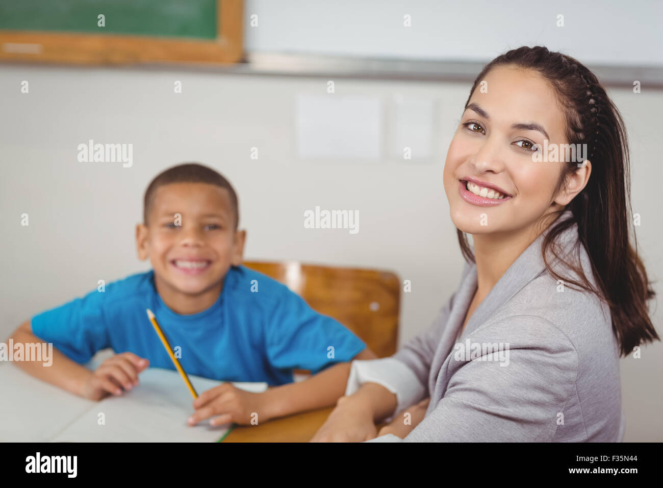 Smiling teacher and her pupil sitting at desk Stock Photo - Alamy