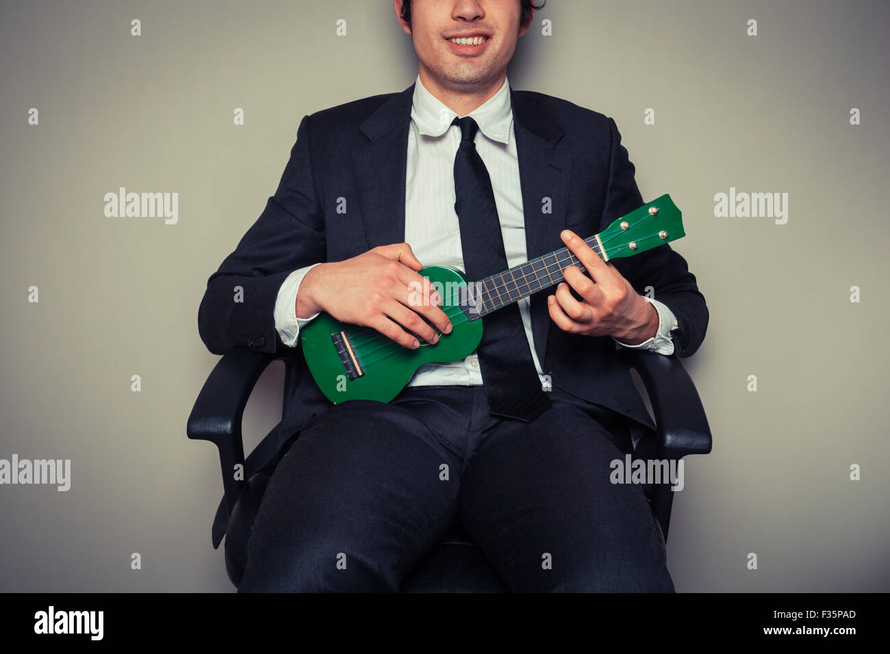 Businessman sitting in an office chair is playing ukulele Stock Photo