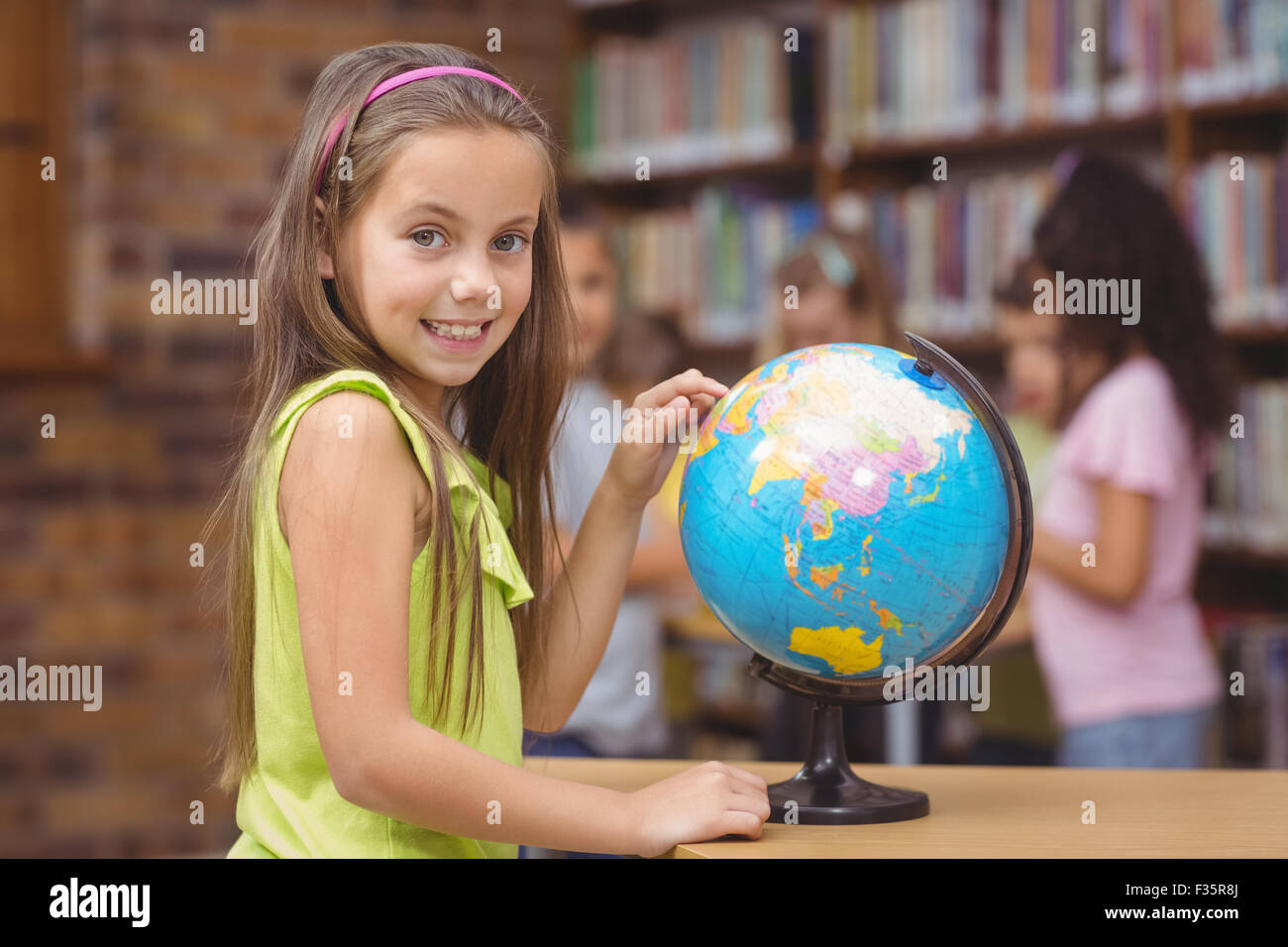 Pupil in library pointing to globe Stock Photo - Alamy