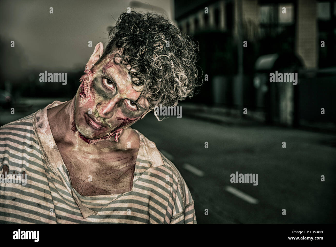 One male zombie standing in empty city street at night looking at camera. Halloween theme Stock Photo