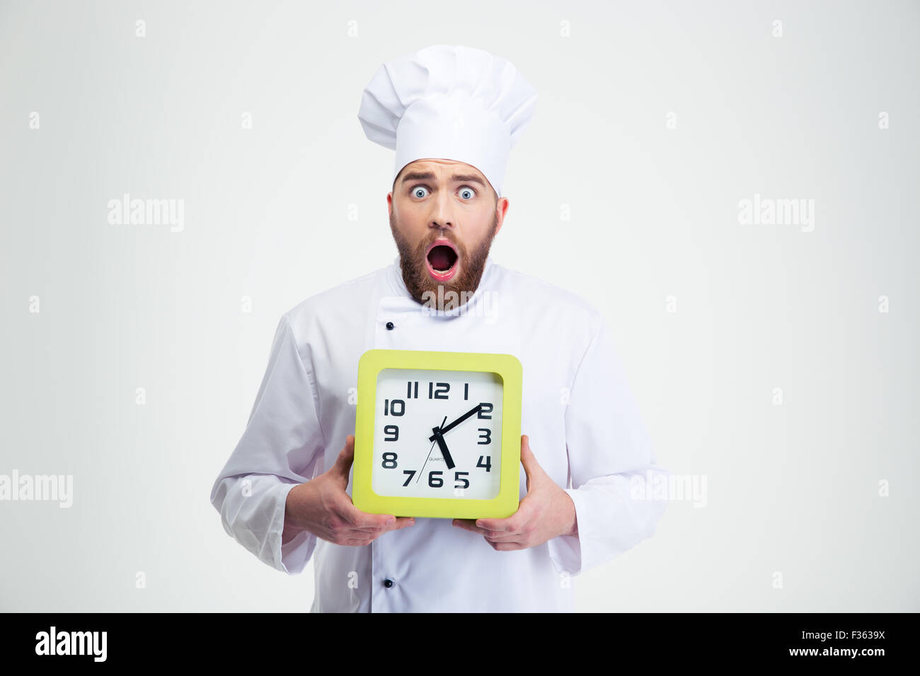Portrait of a shocked male chef cook holding wall clock isolated on a white background Stock Photo