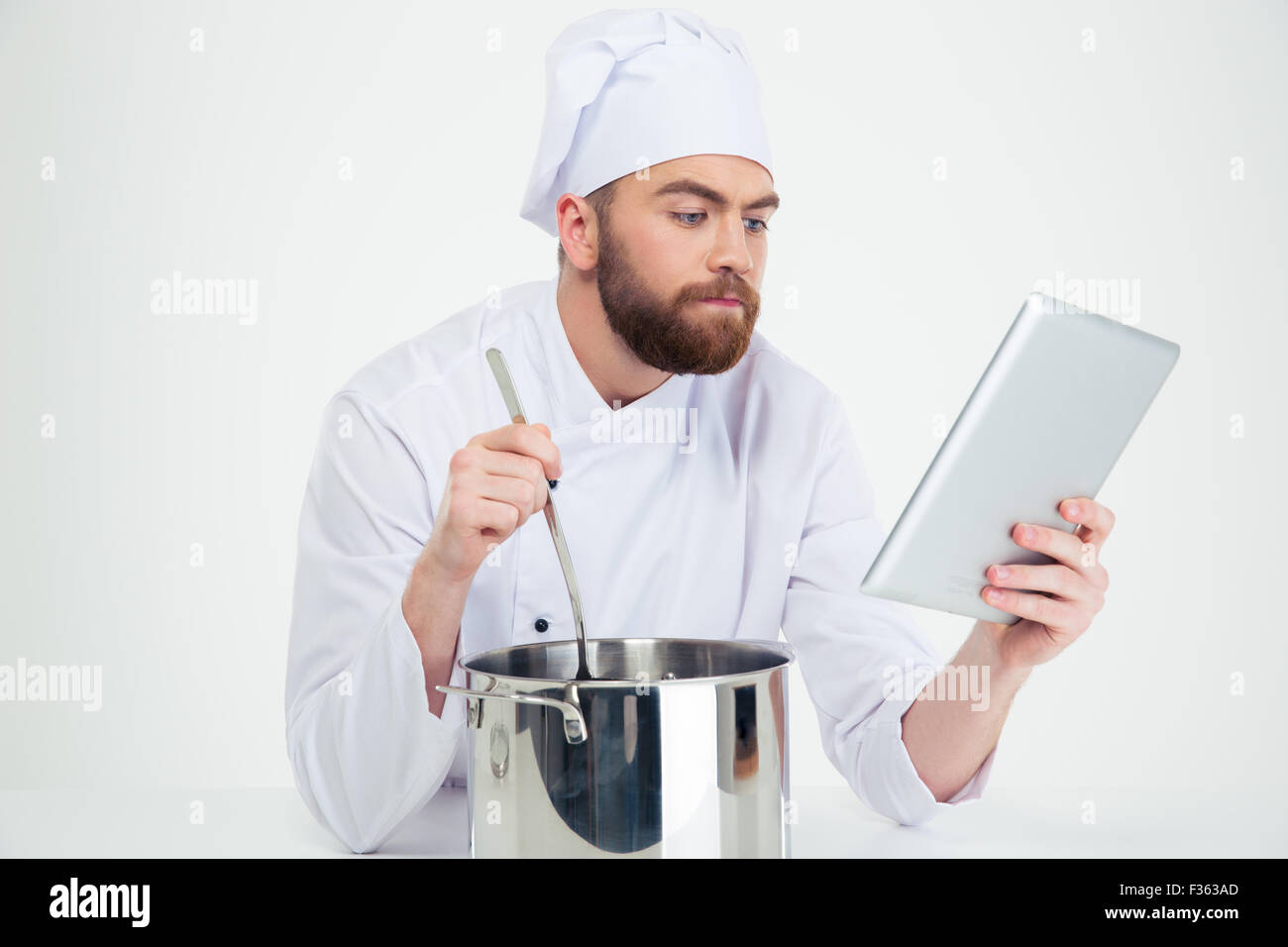 Male chef looking at digital tablet while preparing food isolated on a white background Stock Photo