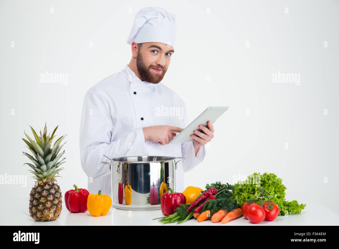 Portrait of a happy male chef cook using tablet computer while preparing food isolated on a white background Stock Photo