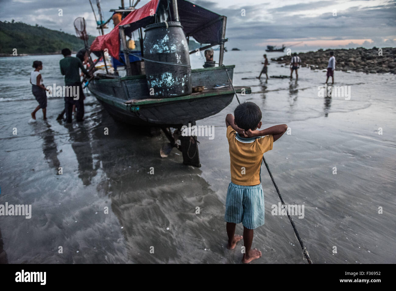 Child by fishing boat, San Hlan beach, Myanmar. Stock Photo