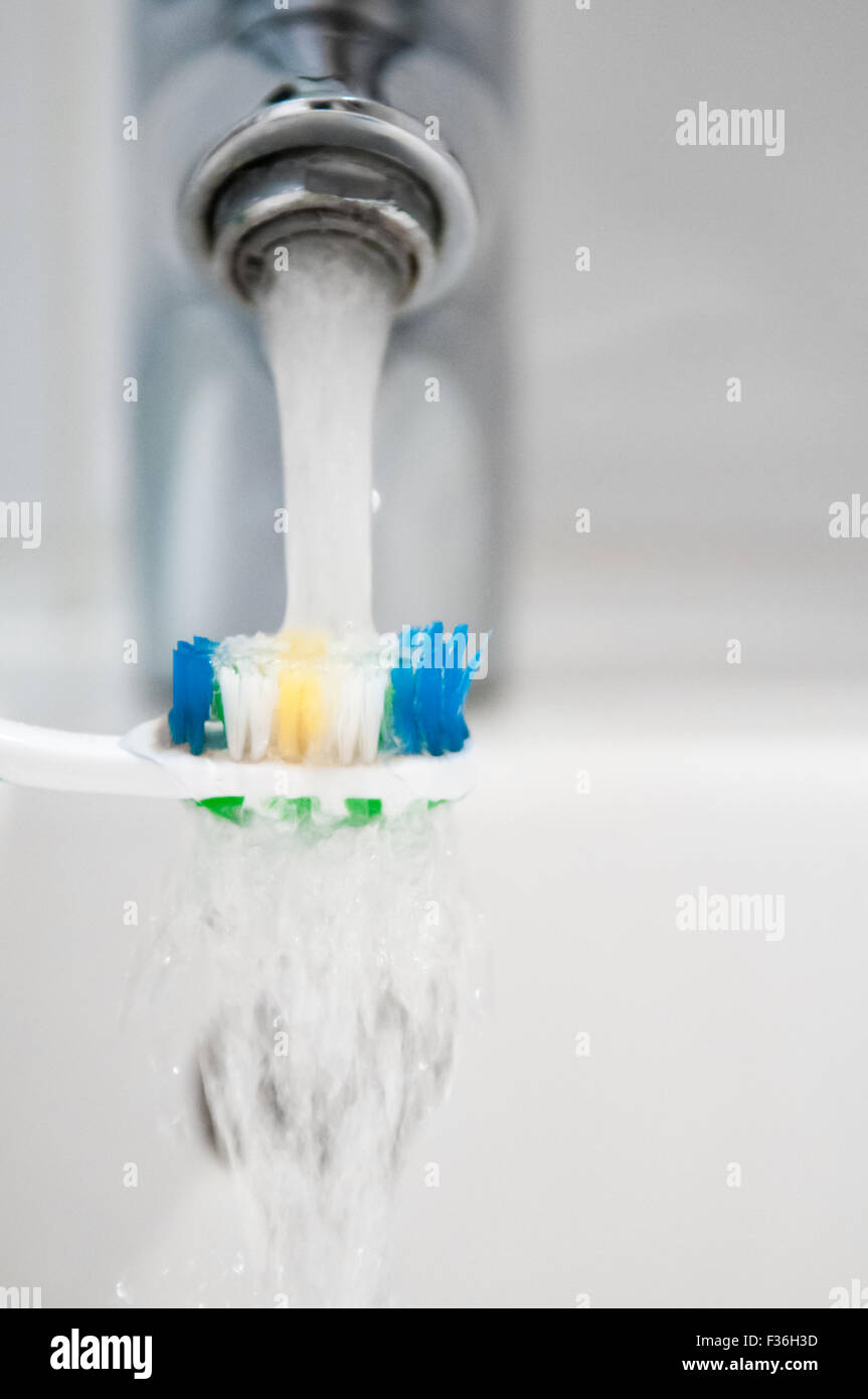 Toothbrush being rinsed under running water from a tap Stock Photo