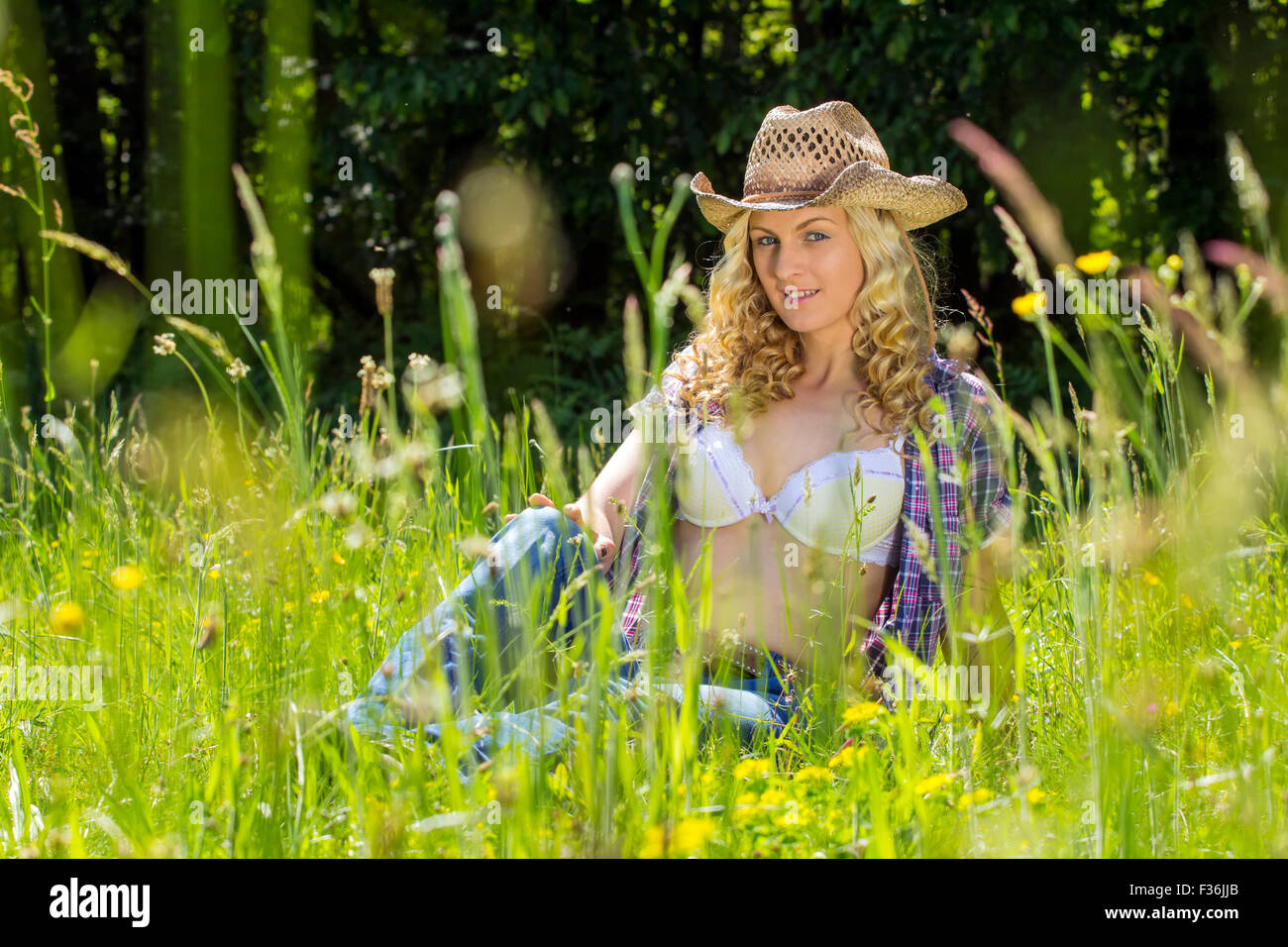 Sexy, blond farmgirl sittin in a tall spring grass. Stock Photo
