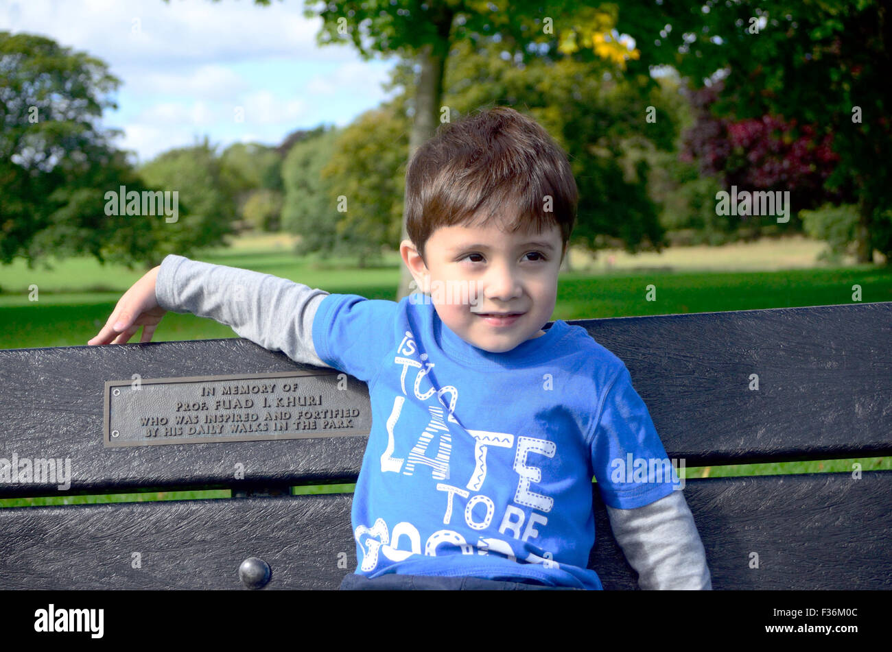 A young boy sits on a bench in the park. Stock Photo
