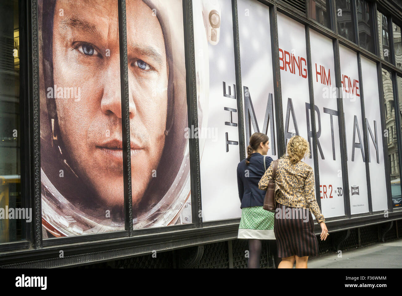 Women walk past the watchful gaze of Matt Damon in advertising in New York for 'The Martian' on Wednesday, September 30, 2015. The film, which is set to open October 2, has been serendipitously promoted by NASA this week with their announcement that they have found running water on Mars.  (© Richard B. Levine) Stock Photo