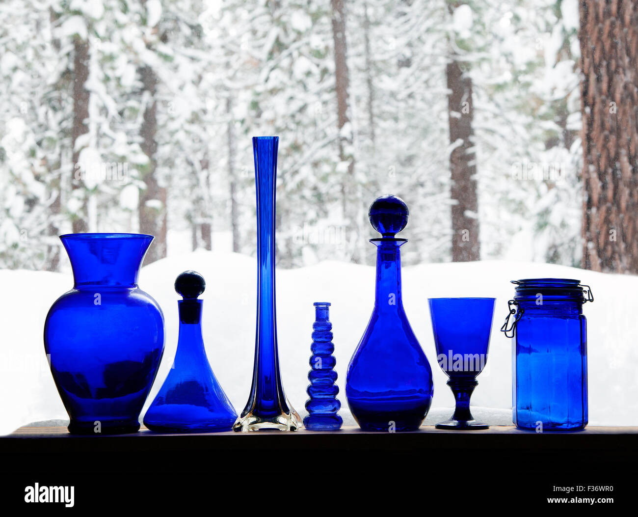 Collection of assorted glowing blue glass bottles  against a snowfall in the forest. Stock Photo
