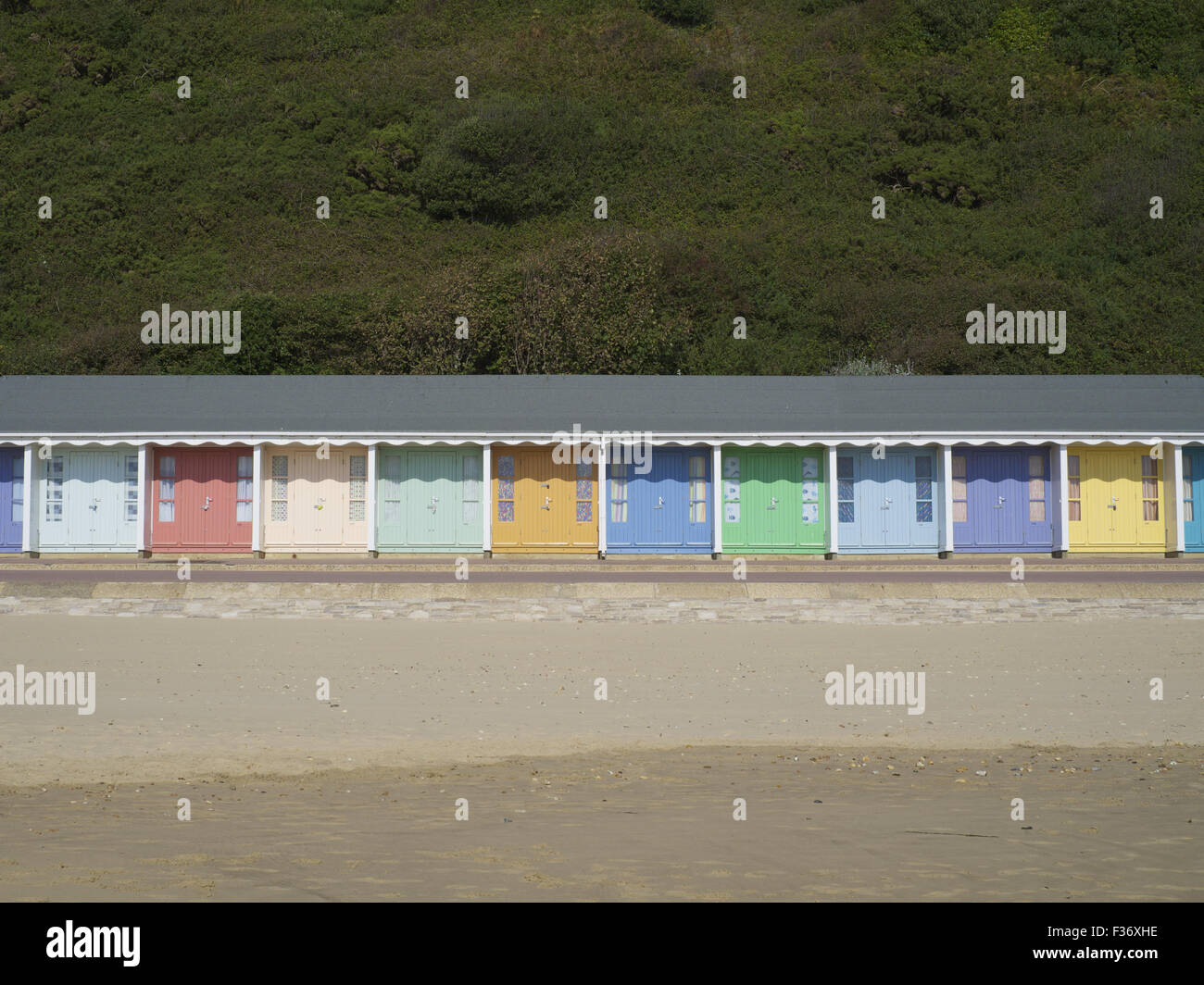 Colourful / colorful beach huts on the south coast of England with yellow sand and green trees. Stock Photo