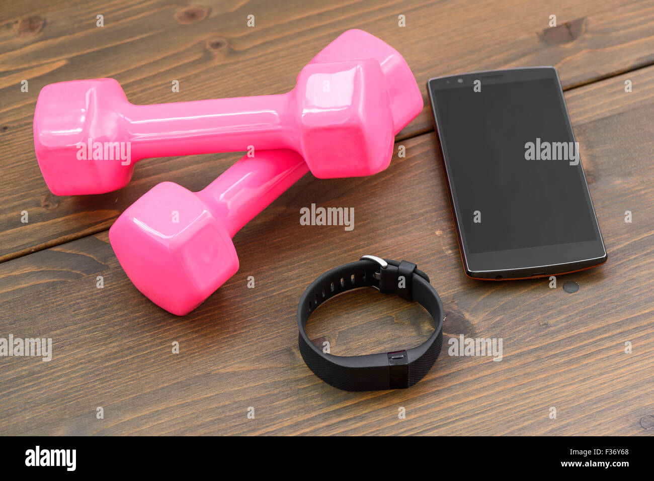 wearable device, wirst watch type Sports tracker with smartphone and pink colored dumb-bell on a wooden board Stock Photo