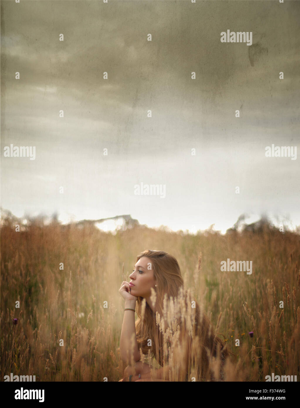 girl sitting between fields with a stormy sky Stock Photo