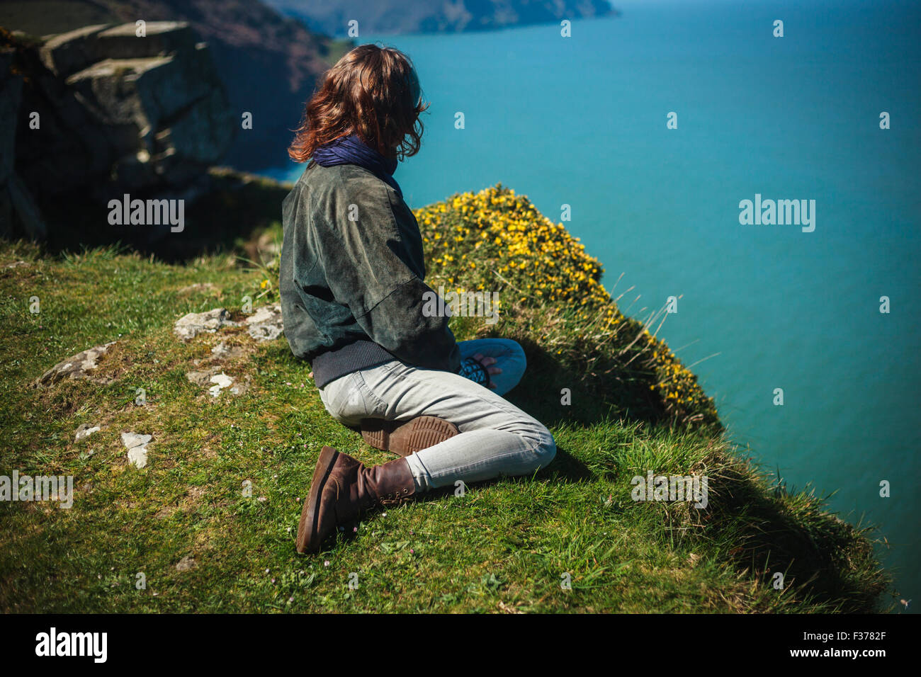 Young woman is sitting on the edge of a cliff by the sea Stock Photo