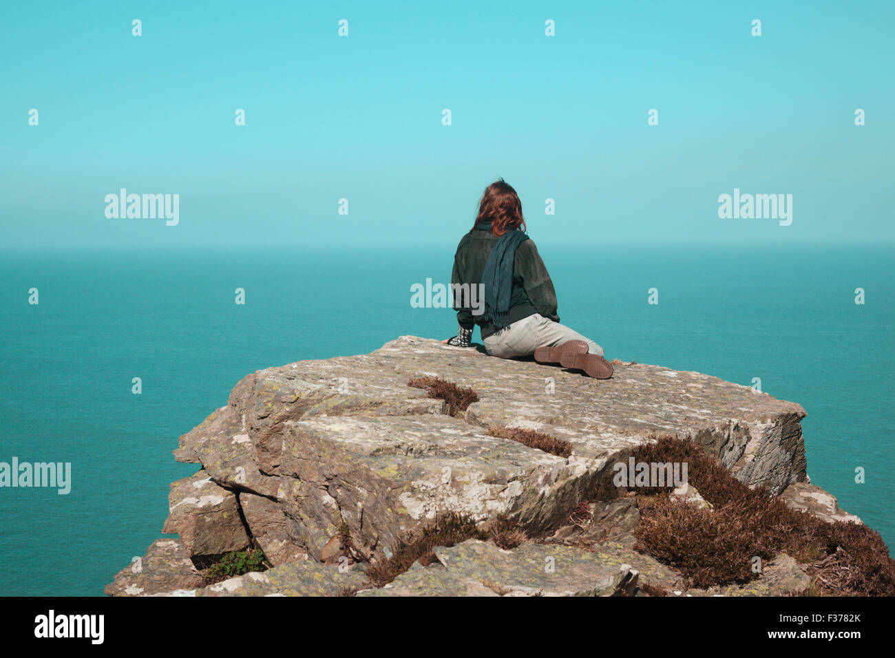 Young woman is sitting on a cliff by the sea Stock Photo