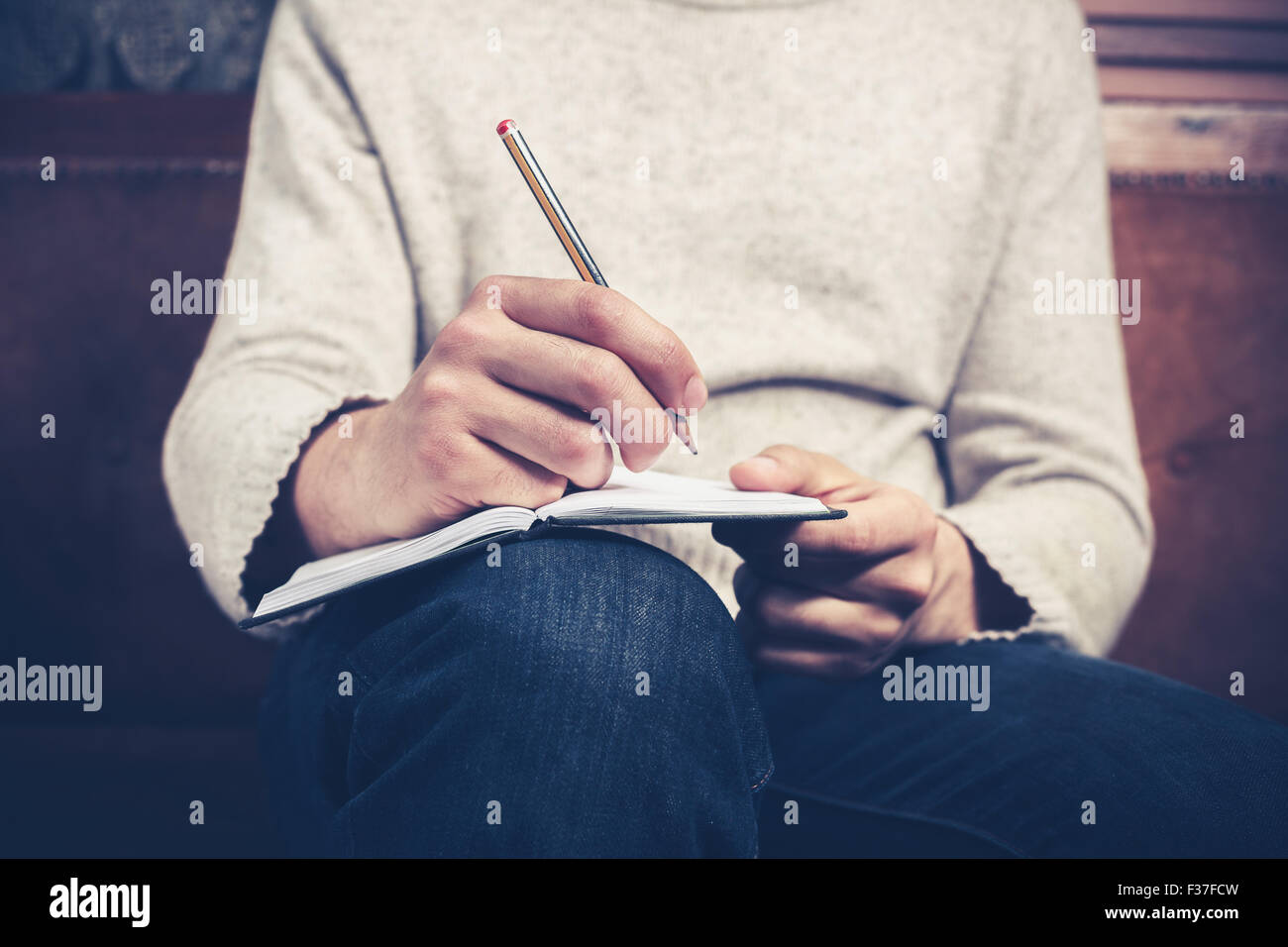 A man is sitting on a sofa and writing notes in a notebook Stock Photo ...