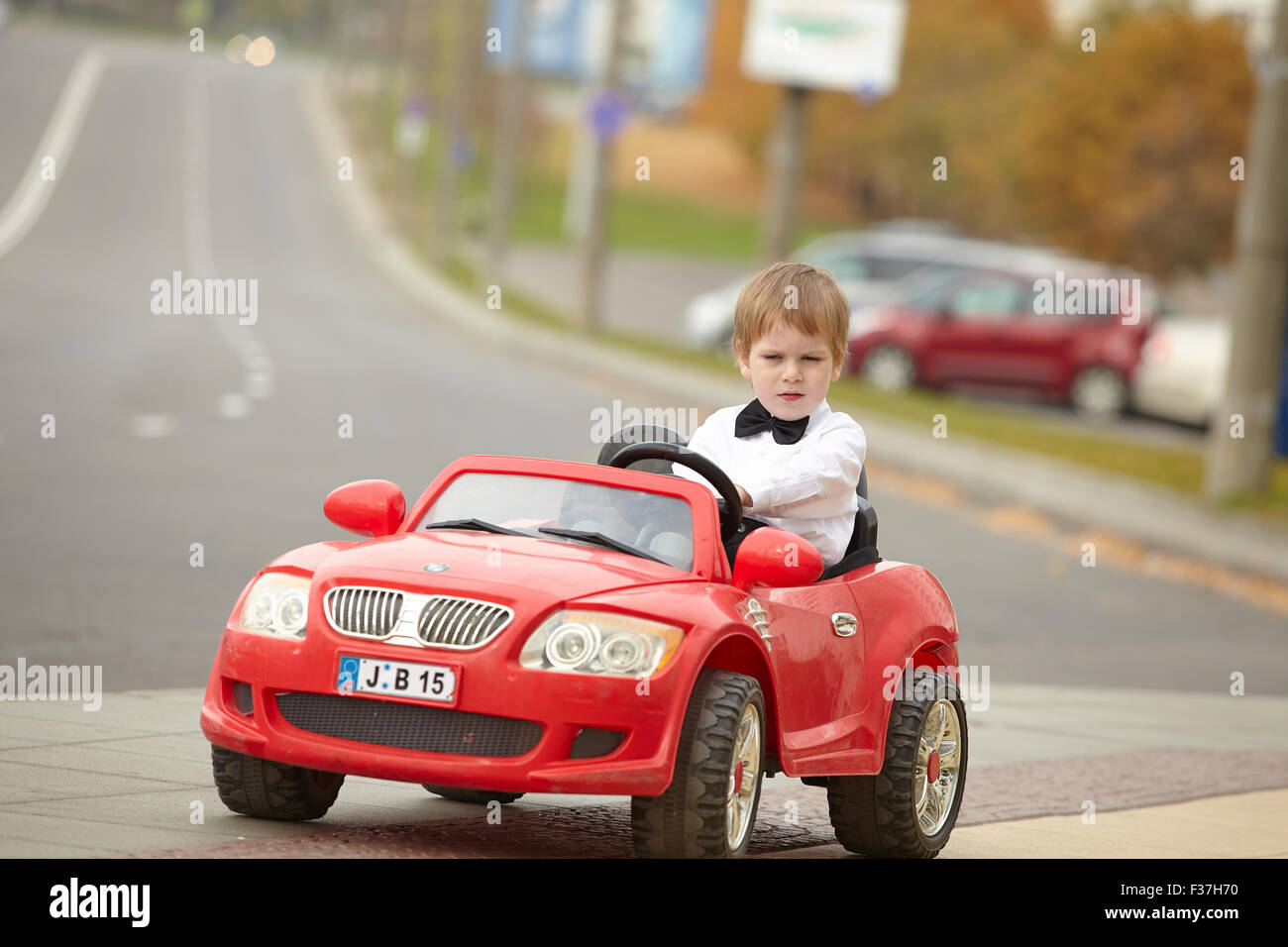 year-old boy in a white shirt in a red toy car in the street Stock ...