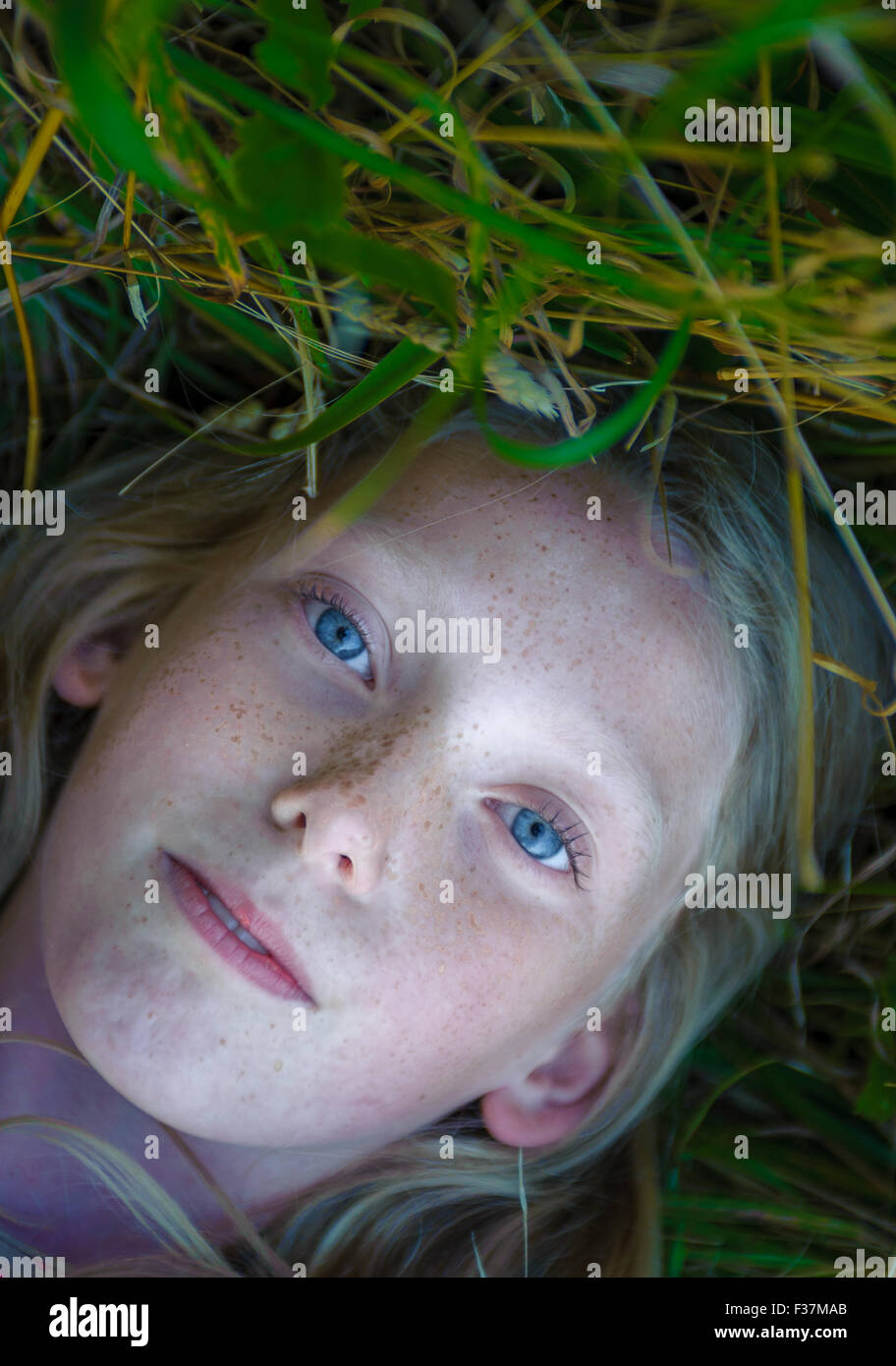 Portrait of a pale faced eight year old girl laying on her back in a field of grass Stock Photo