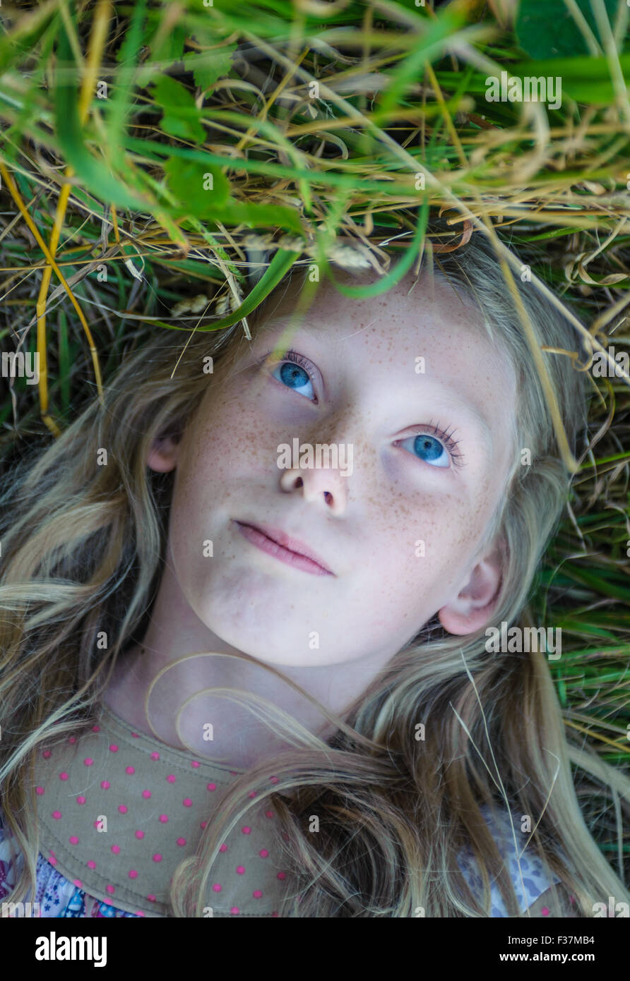 Portrait of a pale faced eight year old girl laying on her back in a field of grass Stock Photo