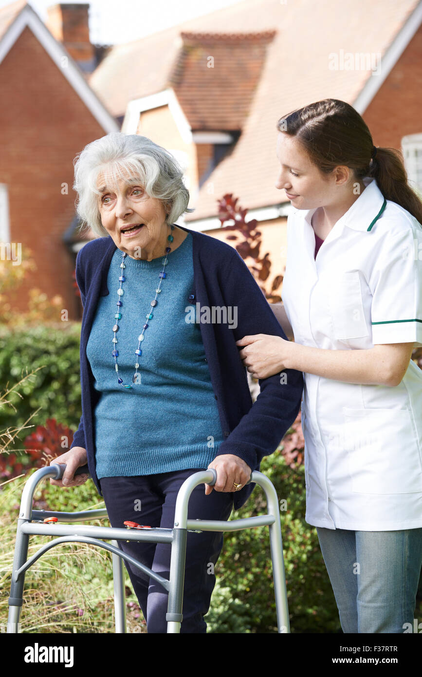 Carer Helping Senior Woman To Walk In Garden Using Walking Frame Stock Photo