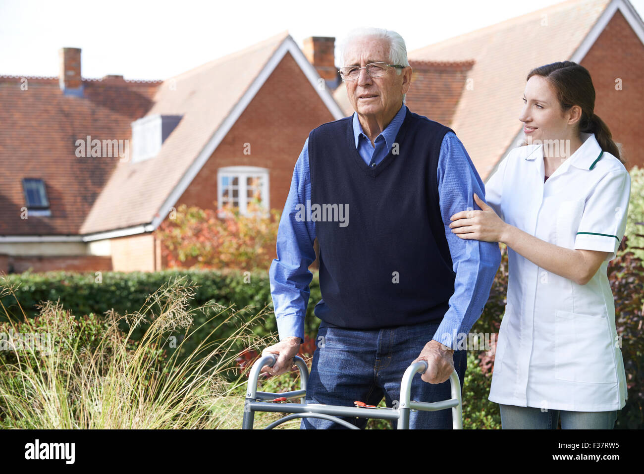 Carer Helping Senior Man To Walk In Garden Using Walking Frame Stock Photo