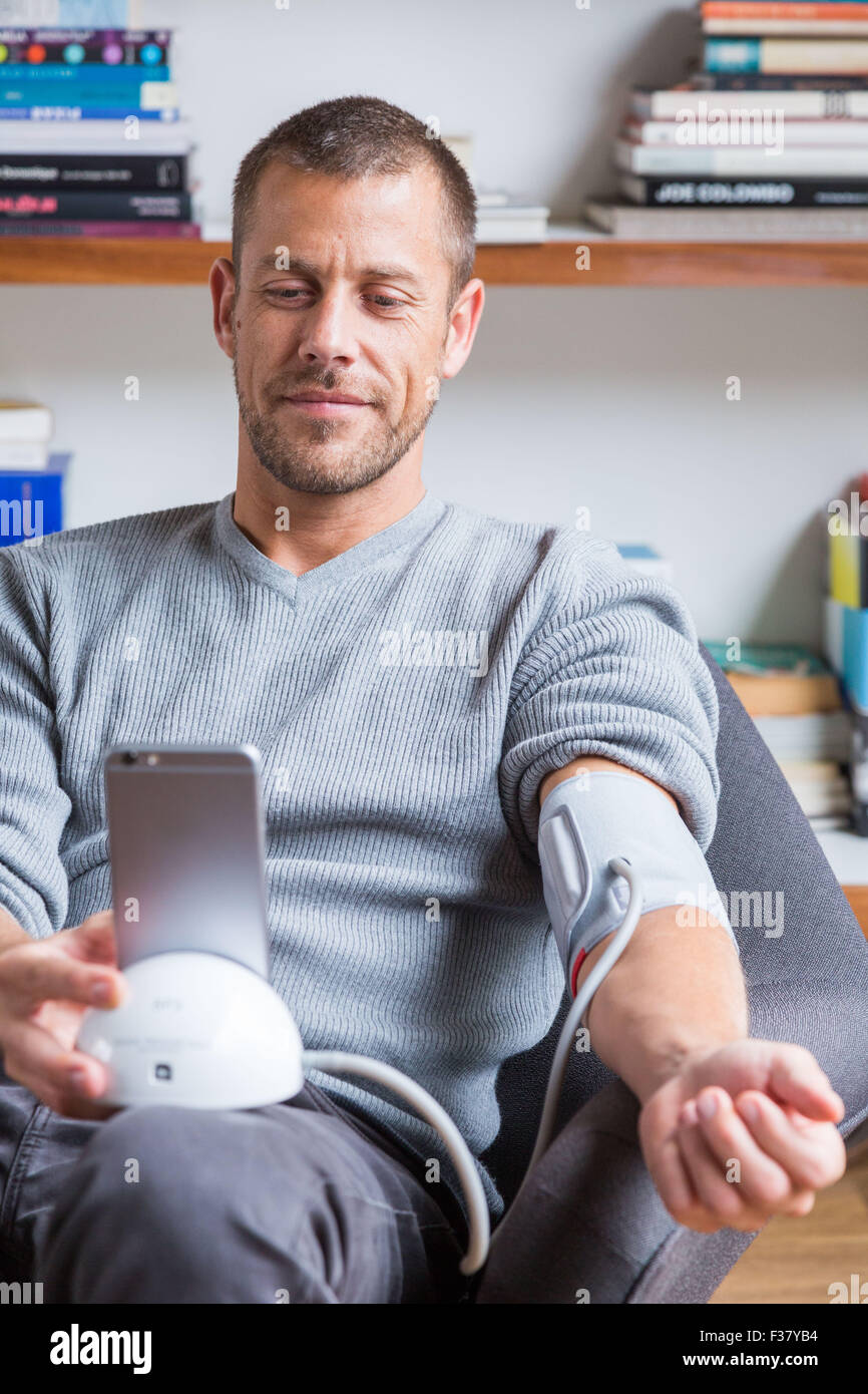 Man taking his blood pressure with a sphygmomanometer connected to his cell phone. Stock Photo