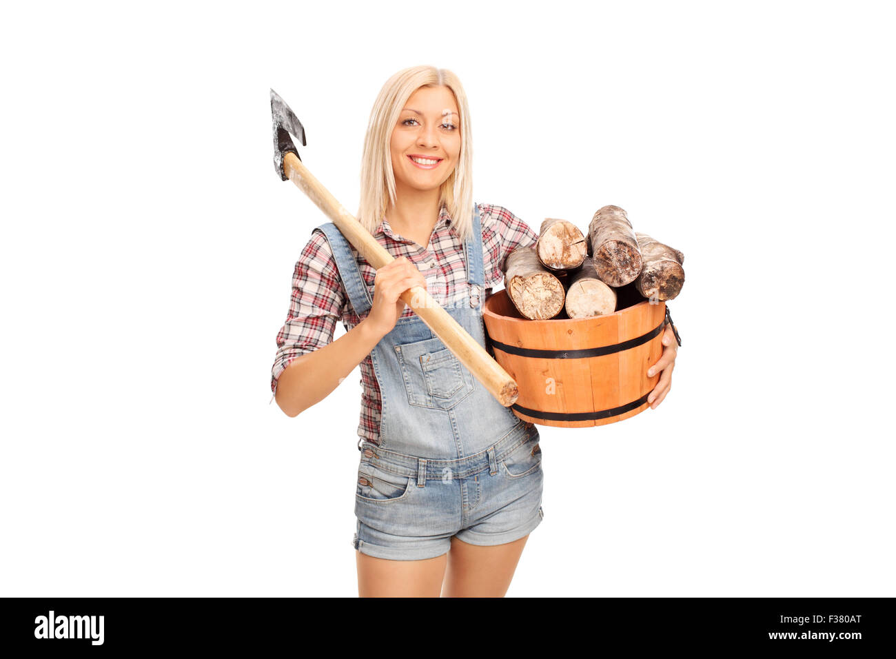 Young blond woman in checkered shirt holding a bucket full of logs and carrying an ax over her shoulder Stock Photo