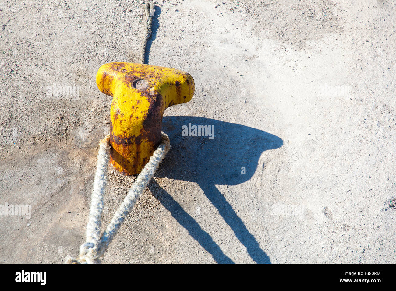 Strong metal mooring bollard with a ship safety rope on a concrete pier. Stock Photo