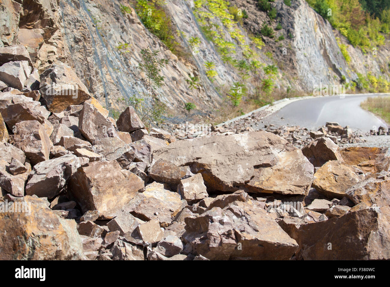 Image of a closed road by a pile of fallen big and small stones. This dangerous accident is caused by a landslide. Stock Photo