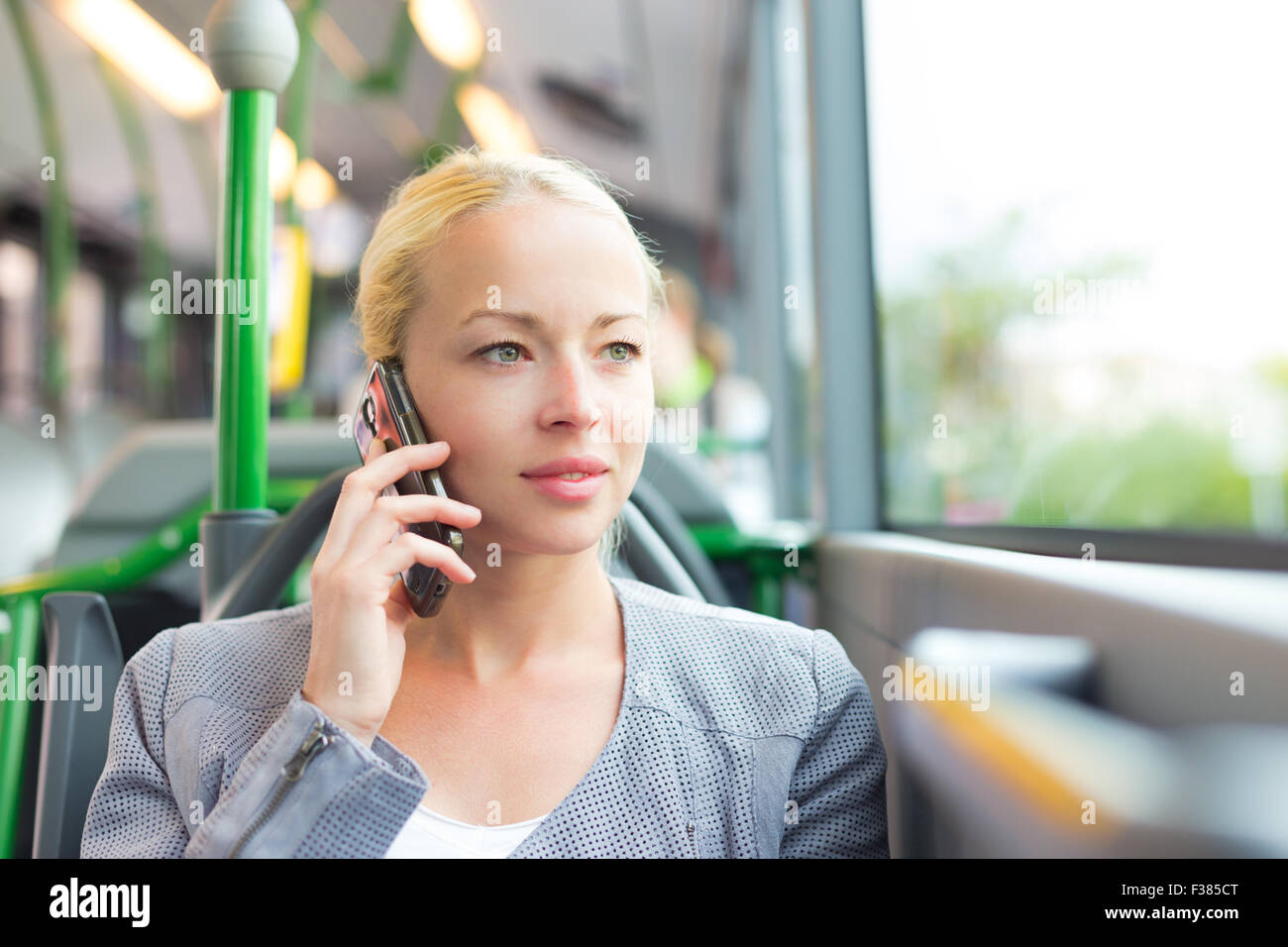 Blonde caucasian business woman talking on cell phone, traveling by bus. Public transport and commuting to work. Stock Photo