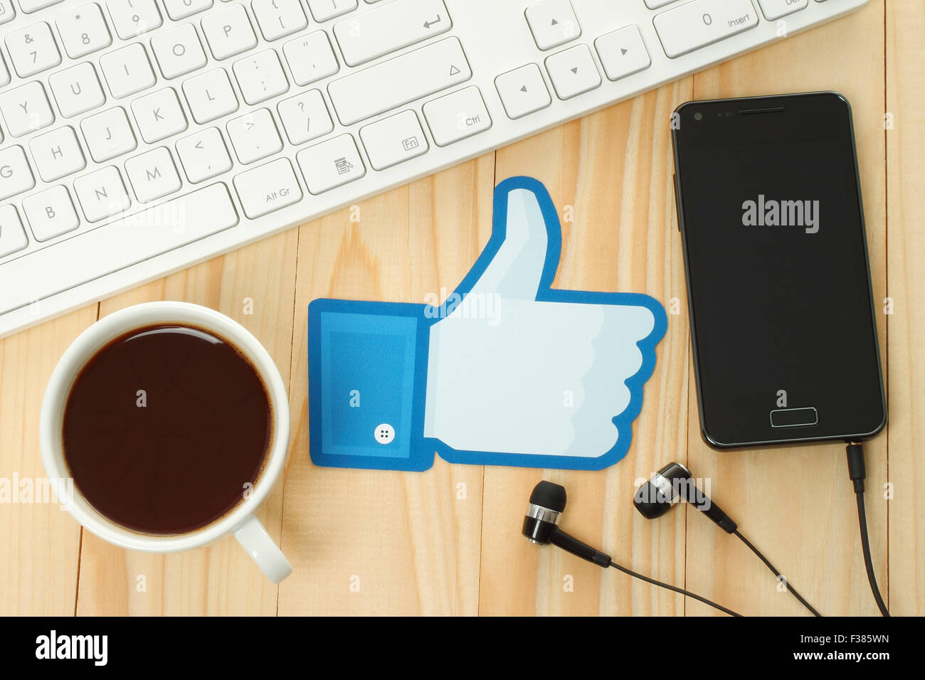 KIEV, UKRAINE - JANUARY 10, 2015: Facebook thumbs up sign printed on paper and placed on wooden background with coffee Stock Photo