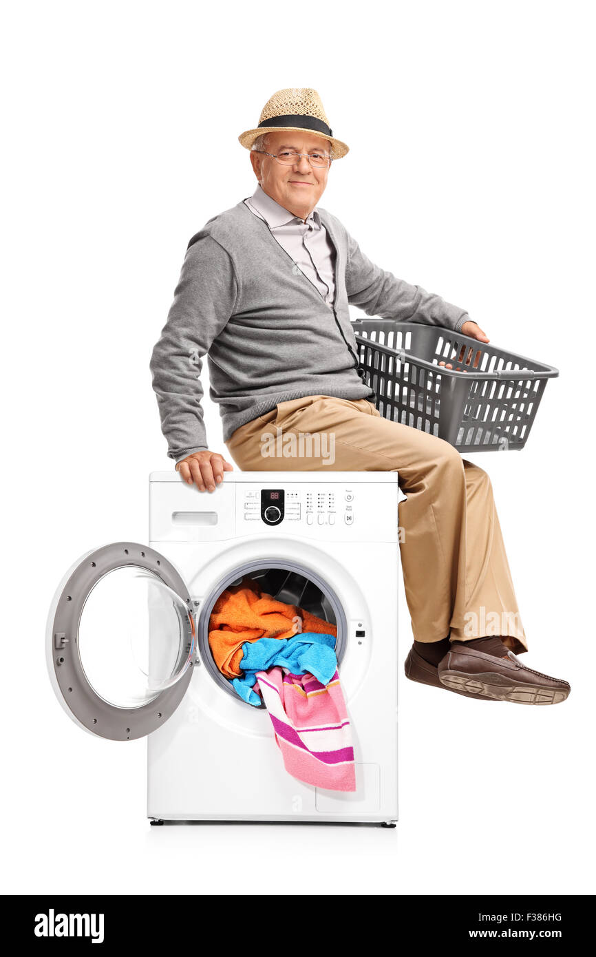 Vertical shot of a senior gentleman sitting on a washing machine and waiting for the laundry isolated on white background Stock Photo